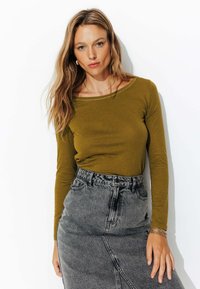 Chemise à manches longues vert olive avec un col large, portée avec une jupe en denim grise taille haute présentant une couture diagonale.