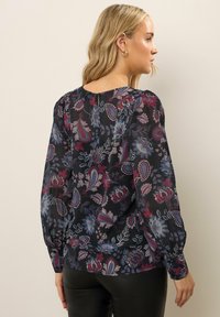 Blusa a maniche lunghe in delicato tessuto nero con motivo floreale colorato in rosso, blu e bianco, colletto tondo e chiusura con bottoni.