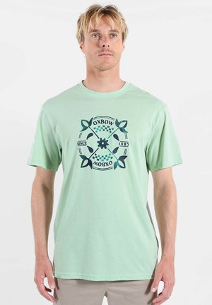 T-shirt en coton vert menthe avec un graphisme circulaire bleu foncé comprenant des feuilles et du texte, manches courtes, coupe décontractée.