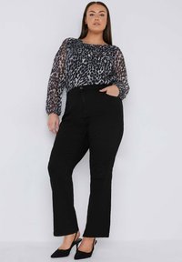 Transparente Bluse mit langen Ärmeln im grau-schwarzen Leopardenmuster; kombiniert mit schwarzen geraden Hosen und schwarzen Slingback-Absatzschuhen.