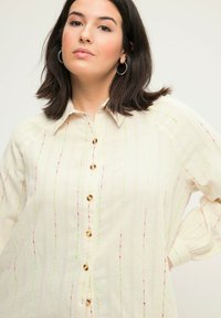 Camicia button-up color crema con ricami verticali colorati in rosa, verde e arancione; presenta un colletto e una vestibilità rilassata.