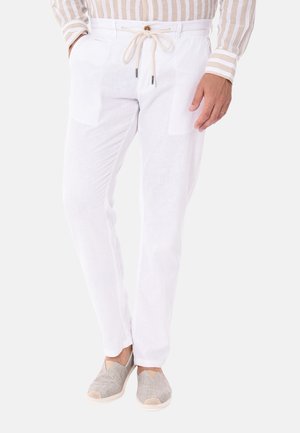 Pantaloni in lino bianchi con due tasche frontali, vita con coulisse regolabile e tessuto leggero. Abbinati a scarpe beige senza lacci.