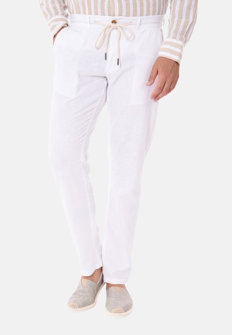 Pantaloni in lino bianchi con due tasche frontali, vita con coulisse regolabile e tessuto leggero. Abbinati a scarpe beige senza lacci.