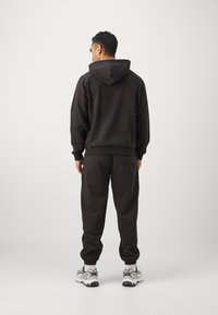 Black cotton hooded sweatshirt and matching joggers, featuring ribbed cuffs and elastic waistband, paired with grey and white sneakers.