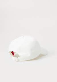 White cotton baseball cap, curved brim, adjustable strap with metallic buckle, featuring a red label inside. Smooth texture and simple design.