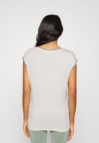 T-shirt às riscas em cinza claro com detalhes em verde, com mangas curtas e uma textura suave, usado com leggings verdes coordenadas.