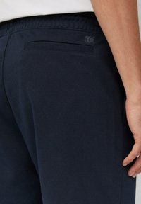 Navyblauwe broek van gestructureerde stof, met een elastische tailleband, een achterzak en een klein logo-detail nabij de zak.