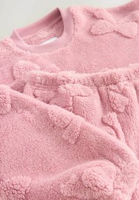 Fuzzy rosa tröja gjord av mjukt material, med en ribbad krage och texturerade accenter formade som rosetter i hela tröjan.