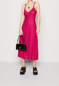 Fuchsia ärmlös klänning med djup V-ringning, svävande silhuett, kombinerad med kraftiga svarta plattformssandaler och en liten svart handväska.