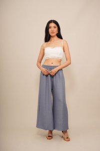 Haut court blanc avec bord en dentelle, associé à un pantalon ample de couleur bleu clair. Le mannequin se tient avec les mains sur les hanches, portant des sandales dorées.