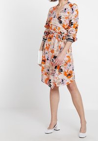 Blommig omlottklänning i lätt tyg med orange och svarta blommor på en rosa bakgrund, långa ärmar och ett design med åtsittande midja.