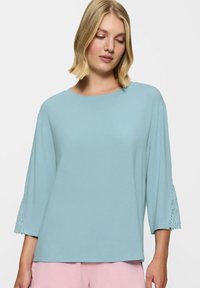 Jasnoniebieska bluzka z długim rękawem, okrągłym dekoltem i koronkowym wykończeniem rękawów, wykonana z miękkiego materiału, w luźnym kroju.