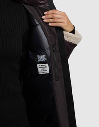 Kurtka puchowa z czarną warstwą zewnętrzną i miękkim beżowym wnętrzem wyściełanym futerkiem. Zawiera metkę z napisem: "Ciepły uścisk zrobiony z tkaniny."