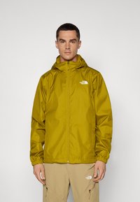 Veste étanche jaune avec fermeture éclair à l'avant et capuche ajustable. Équipée de poignets élastiques et d'un logo sur la poitrine gauche. Matière lisse et légère.