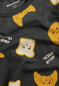 Schwarzes T-Shirt mit verspielten Lebensmittelmustern, einschließlich lächelndem Toast und Croissant, mit dem Text „Hallo dort“ in Weiß. Aus weichem Baumwollmaterial.