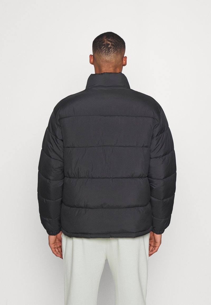 Schwarze gepolsterte Jacke mit hohem Kragen, gesteppter Optik und elastischen Bündchen, die eine glatte, glänzende Textur bietet. Rückansicht.
