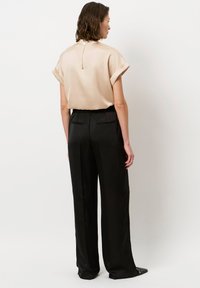 Beige satin Kurzarm-Top mit hohem Kragen und Reißverschluss, kombiniert mit schwarzen, weit geschnittenen Hosen mit Taillenbund und Gesäßtaschen.