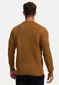 Brown sweater with a herringbone pattern, ribbed cuffs and hem, and a crew neckline, made of thick, textured knit fabric.