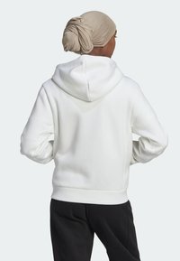 Sweatshirt à capuche blanche avec une texture douce, présentant une coupe décontractée et une capuche ajustable, associé à un pantalon noir.