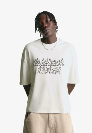 White oversized t-shirt made of cotton, featuring a black embroidered text design that reads "laidback stories." Short sleeves and relaxed fit.