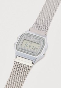 Digital Casio-ur med en rektangulær sølvfarvet urskive, vandafvisende funktion og en rustfri stål mesh-rem. Skærmen viser tid og dato.