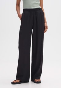 Svarta vida byxor med elastisk midja, tillverkade av lätt tyg, med en slät yta och en lätt draperad passform.