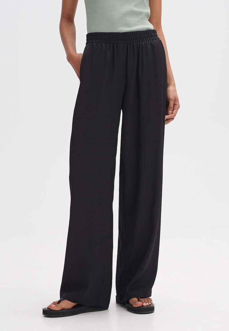 Svarta vida byxor med elastisk midja, tillverkade av lätt tyg, med en slät yta och en lätt draperad passform.