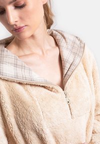 Zipperowa polarowa kurtka w jasnym beżu o miękkiej fakturze, z kapturem w kratę w neutralnych odcieniach i półzamkiem z przodu.