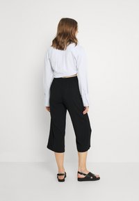 Ljusblå cropped knäppskjorta, svarta lösa culotter och svarta sandaler med glansiga remmar. Slät tyg och avspänd silhuett.