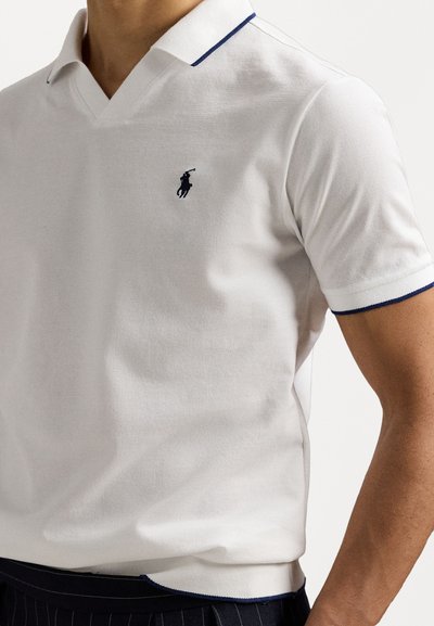 Polo shirt blanc à manches courtes, en tissu tricoté, avec un design en V, mettant en valeur des accents de col bleu marine et un petit logo sombre sur la poitrine.