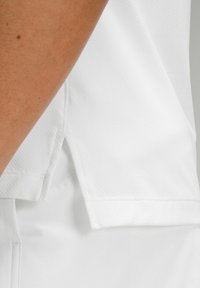 Bijela atletská majica sa teksturiranim materijalom, kratkim rukavima i bočnim prorezima na rubu za poboljšanu pokretljivost.