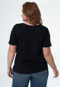 Haut noir à manches courtes avec une coupe décontractée, un col rond et un tissu en coton lisse, associé à un jean en denim bleu clair.