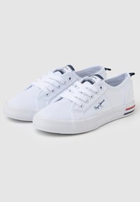Sneakers in tela bianca con suole in gomma, punta rotonda e chiusura con lacci. Presentano un accento blu sul tallone e un dettaglio rigato sul lato.