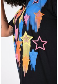 Sort t-shirt med farverige stjerne-grafikker i blå, pink, orange og gul med dryp-effekter. Korte ærmer, afslappet pasform.