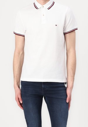 Weißes Poloshirt mit zweiknöpfiger Knopfleiste, kontrastierendem rot-blau gestreiftem Kragen und Ärmeln, mit kleinem Logo auf der Brust.