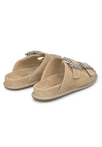 Beige Wildleder Slipper-Sandalen mit dekorativer Hardware in Silberfarbe und einer erhöhten Sohle, die eine glatte Textur und ein offenes Rückendesign aufweisen.