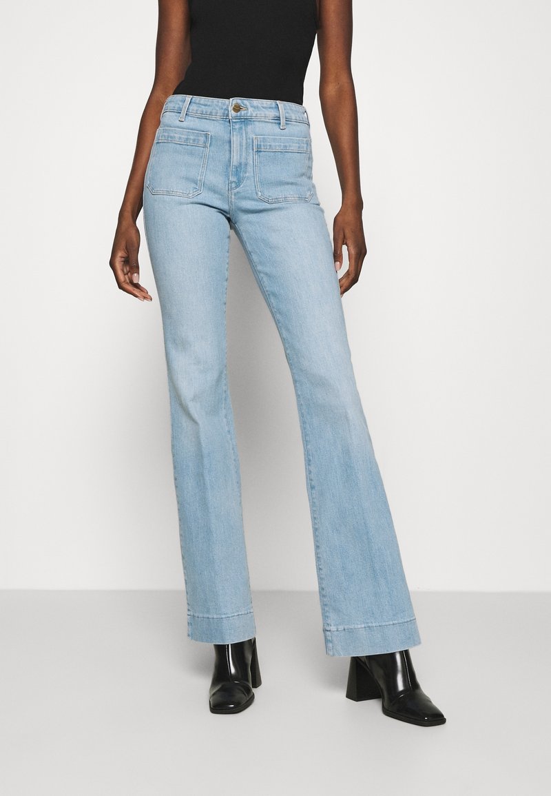 Hellblaue, ausgestellte Jeans aus Denim mit hoher Taille, zwei Gesäßtaschen und einem Knopfverschluss. Kombiniert mit schwarzen Knöchelstiefeln.