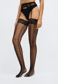 Sorte strømpebukser til låret med blondetopp med blomsterdesign og fiskenettstruktur, som fremhever intrikate vertikale mønstre.