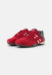 Scarpe da ginnastica rosse in suede con tomaia in rete, accenti grigi e suola in gomma testurizzata con strisce bianche sui lati.