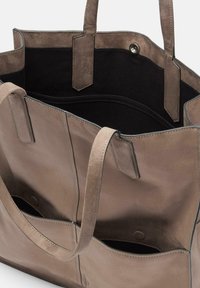 Taupe suède tote bag met twee buitenzakken, zwarte stoffen voering en dubbele open bovenkant. Kenmerkend zijn de stikselaccenten en de korte handvatten.