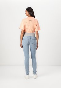 Camiseta corta de manga corta en color rosa con una cinturilla gris, combinada con jeans ajustados de color azul claro. La parte posterior de la camiseta tiene el texto: "EVERY DAY."