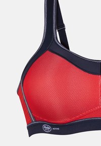 Soutien-gorge de sport rouge en tissu texturé, avec des accents marins et des bretelles ajustables. Comprend un détail de logo sur la bande.
