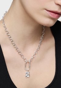 Srebrny naszyjnik łańcuszkowy z owalnymi ogniwami i pendantem w kształcie niedźwiedzia z dwoma czarnymi akcentami. Minimalistyczny design z polerowanym wykończeniem.