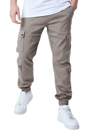 Pantalones cargo de color marrón claro con puños elásticos, que cuentan con múltiples bolsillos laterales y botones a presión, combinados con zapatillas blancas.