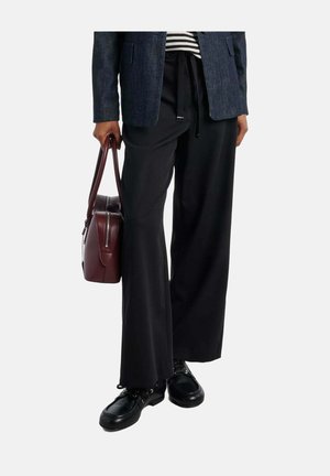 Persoon die zwarte broek met wijde pijpen draagt, zwarte veterschoenen, gestreept topje, donkerblazer, en een donkerrode aktetas-handtas vasthoudt.