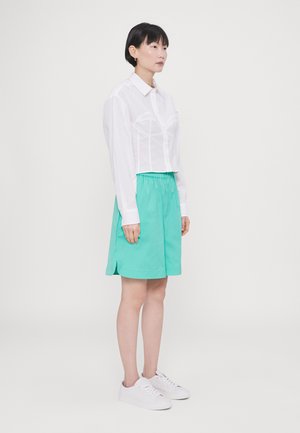 Kort hvid skjorte med knaplukning, der har et struktureret design; parret med en mintgrøn A-line nederdel og hvide sneakers.