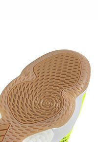 Suela de zapato con una superficie de goma texturizada en color marrón y características cortes circulares y ovalados. Acentos en blanco y un vibrante color amarillo en la parte superior.