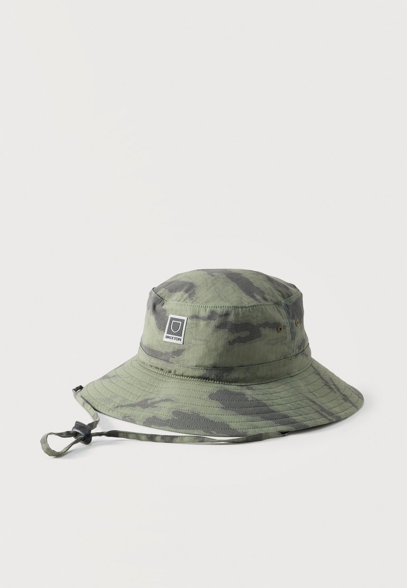 Πράσινο και γκρι καμουφλάζ καπέλο τύπου bucket με φαρδύ γείσο, ρυθμιζόμενο λουρί κάτω από το πηγούνι και ένα μικρό ορθογώνιο λογότυπο στο μπροστινό μέρος.
