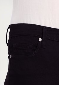 Vaqueros de mezclilla negra con una cintura de altura media, bolsillo frontal y detalles en metal plateado en el cinturón y el bolsillo. Tejido texturizado.