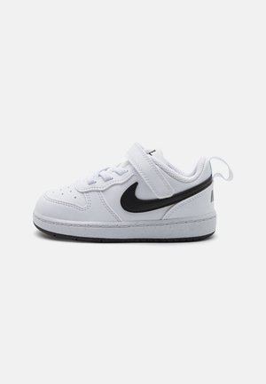 White leather sneaker with a black Nike swoosh, lace and strap closure, textured interior, and black rubber sole, featuring a pull tab.